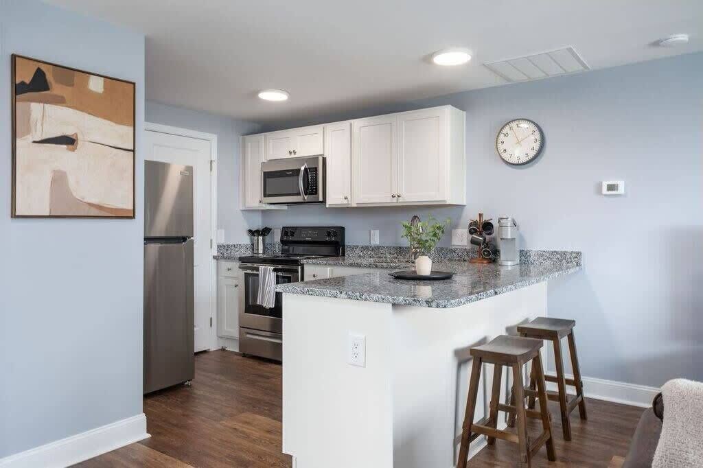 A modern kitchen with white cabinets, a granite countertop, stainless steel appliances, and a clock on the wall.