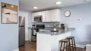 A modern kitchen with white cabinets, a granite countertop, stainless steel appliances, and a clock on the wall.