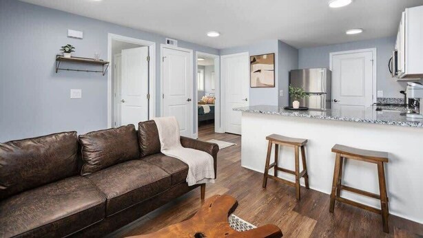 A modern living room with a brown leather sofa, wooden stools, and a kitchen area with a marble countertop.