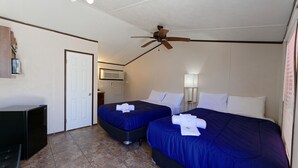 A hotel room with two beds, a ceiling fan, a refrigerator, and a door. - Target Hospitality - Big Spring Lodge (Big Spring)