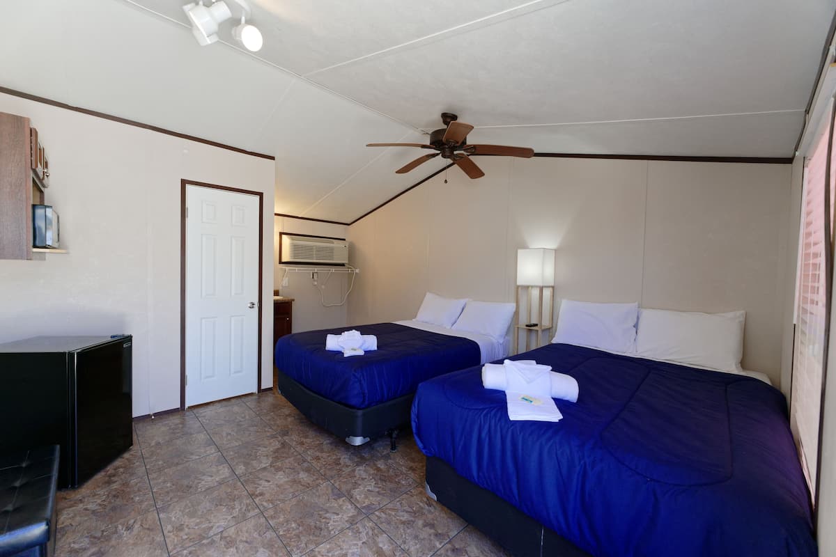 Habitación de hotel con dos camas, ventilador de techo, refrigerador y una puerta.