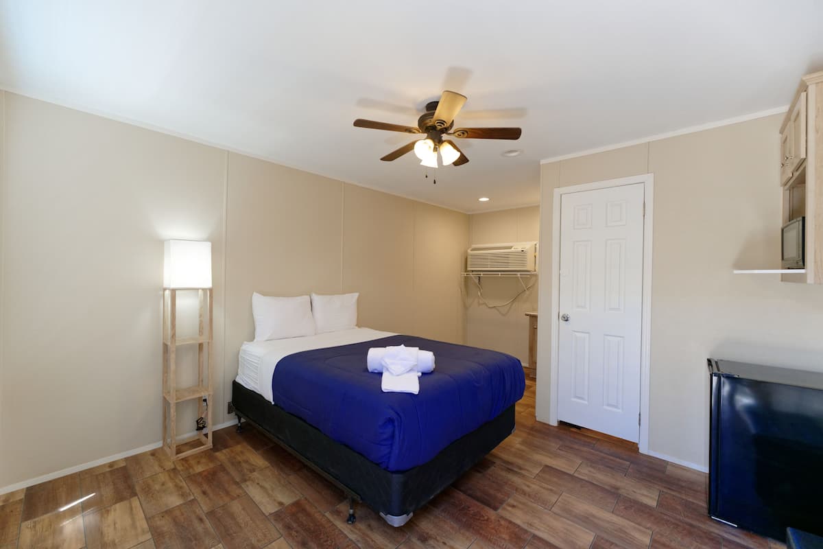 Una habitación de hotel con cama, ventilador de techo, televisor y puerta.