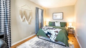 A bedroom with a bed, two bedside tables, a hanging light fixture, and a framed picture on the wall.