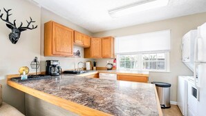 A kitchen with wooden cabinets, a granite countertop, a coffee maker, and a window with blinds.