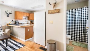 A compact kitchen with wooden cabinets, a built-in fridge, a coffee maker, and a welcome sign.