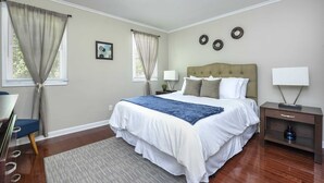 Une chambre à coucher avec un grand lit, deux tables de chevet avec des lampes, un bureau avec une chaise et une fenêtre avec des rideaux.