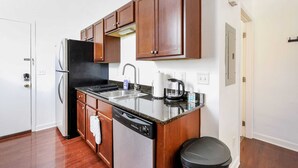 Una cocina compacta con armarios de madera, un refrigerador de acero inoxidable, lavavajillas, un fregadero y una cafetera.