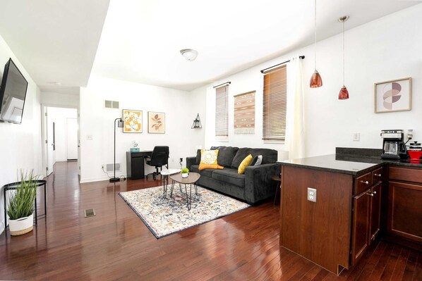 A modern living room with a sofa, coffee table, and a kitchen area with a countertop and cabinets.
