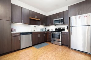 Une cuisine moderne avec des meubles en bois foncé, des appareils électroménagers en acier inoxydable et un plancher en bois.