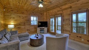 A log cabin interior with a wooden ceiling, a flat-screen TV, a sofa, a round coffee table, and large windows. - Sharin-A-Lakeview | $229 Off Your Stay! (Blue Ridge)
