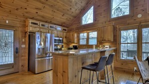 A wooden cabin kitchen with a central island, bar stools, and large windows. - Sharin-A-Lakeview | $229 Off Your Stay! (Blue Ridge)