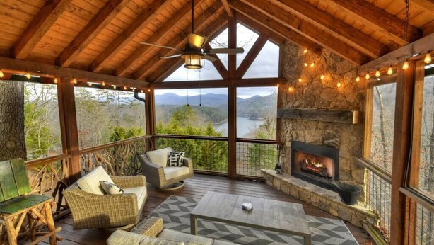 A cozy wooden deck with wicker furniture, a stone fireplace, and a scenic view of a river and mountains. - Sharin-A-Lakeview | $229 Off Your Stay! (Blue Ridge)