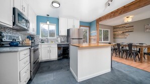 Une cuisine moderne avec des meubles blancs, un îlot central, des appareils électroménagers en acier inoxydable et un coin repas comprenant une table et des chaises en bois.