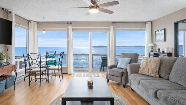 A spacious living room with a view of the sea, a ceiling fan, a dining area with chairs, and a sofa. - Hop off the steps onto the beach - a rare Birch Bay Find!  Kayaks, full kitchen. (Blaine)