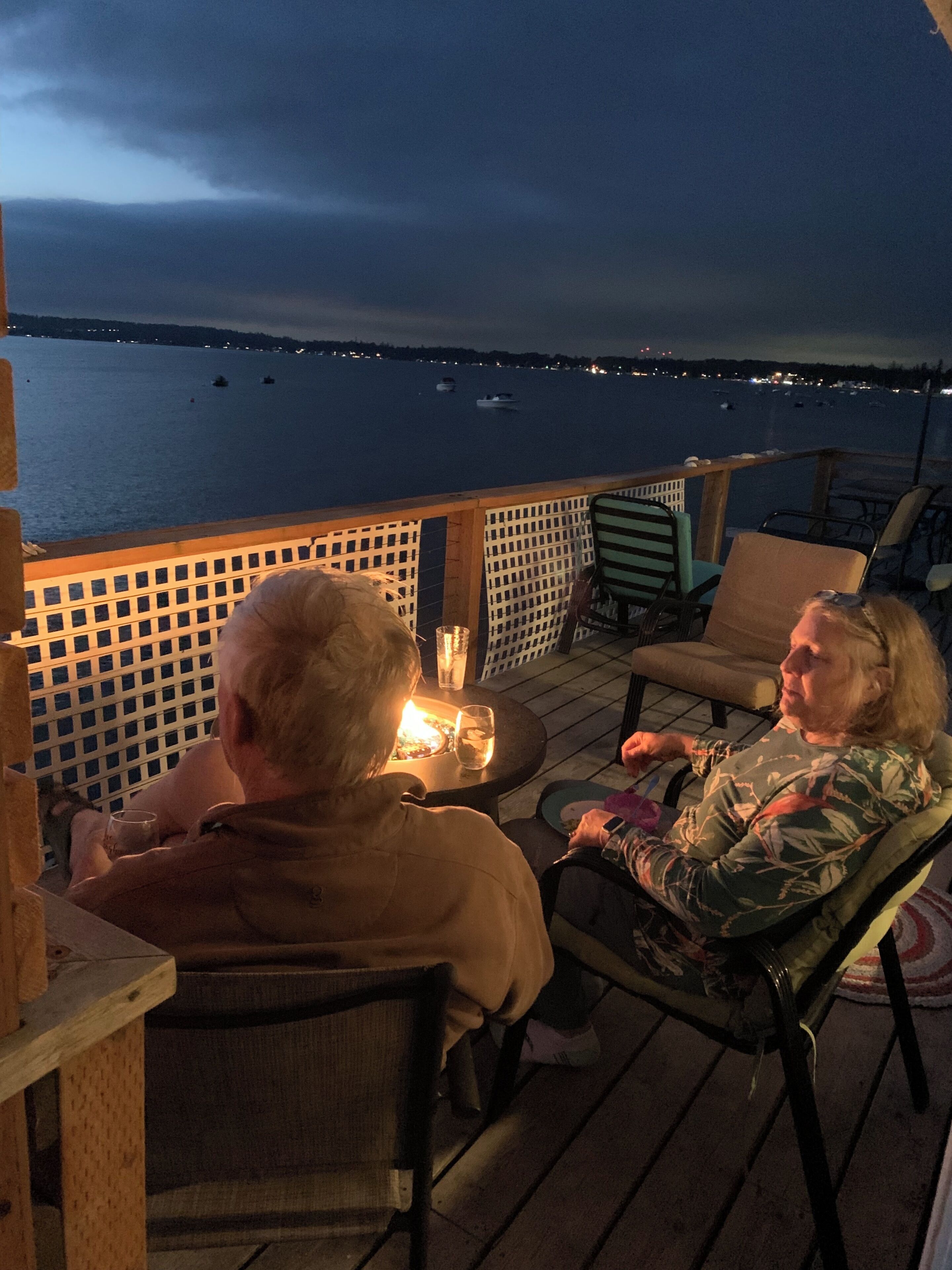 Une terrasse avec deux chaises, une table et une rambarde donnant sur une étendue d’eau où se trouvent des bateaux.