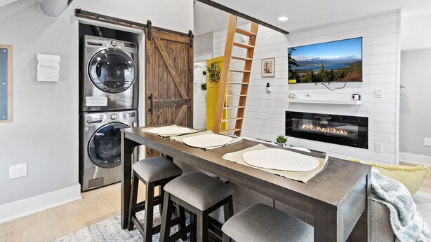 Una cocina moderna con una mesa de madera, taburetes de bar, lavadora y secadora integradas, una chimenea y un televisor montado en la pared.