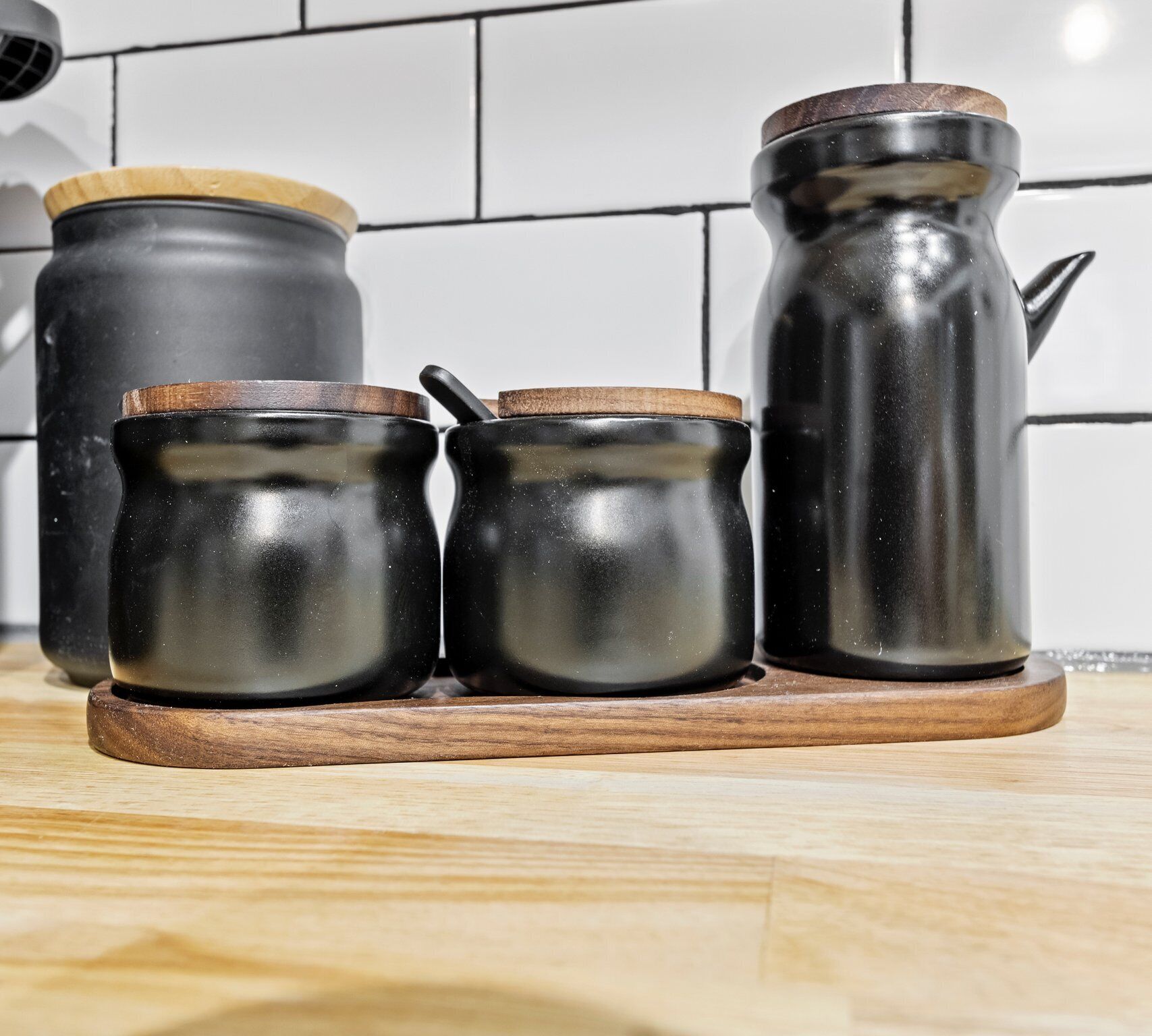 Three black ceramic containers with wooden lids on a wooden tray.