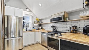 Una cocina moderna con electrodomésticos de acero inoxidable, encimera de madera y salpicadero azulejado.