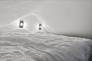 A bedroom with a sloped ceiling, white walls, and two wall-mounted light fixtures.