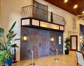 A cinema entrance with a sign reading 'Paradise Palms Cinema,' featuring a wooden facade and a balcony with a metal railing.