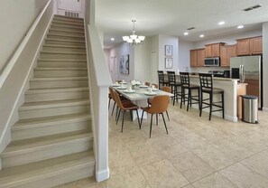 A kitchen with a dining area, a staircase, and a trash can.