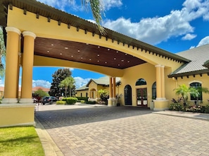 A hotel entrance with a covered walkway, palm trees, and a paved driveway.