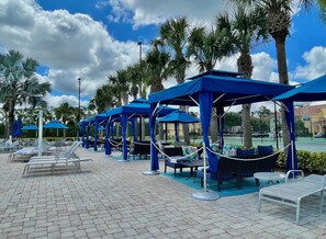 A poolside area with lounge chairs and blue canopies.