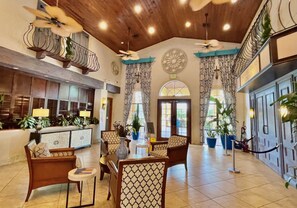 A spacious lobby with a high ceiling, patterned chairs, a reception desk, and a large decorative fan.