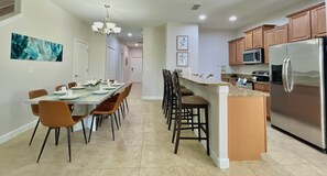 A modern kitchen with a stainless steel refrigerator, a microwave, and a dining area with a long table and chairs.