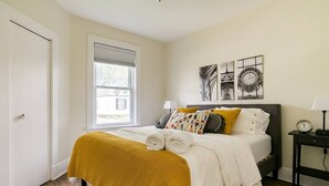Une chambre à coucher bien rangée, avec un lit, des lampes de chevet, une horloge et des œuvres d’art accrochées au mur.
