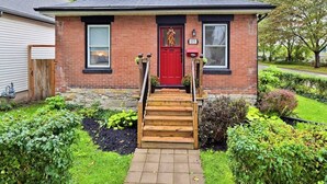 Une maison à deux étages, construite en briques, avec une porte d’entrée rouge, un petit porche et un escalier en bois menant à l’entrée.