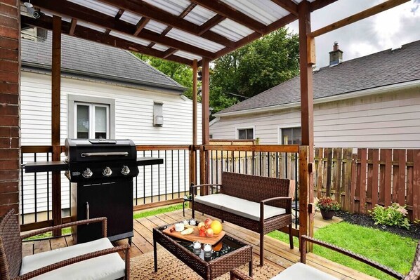 A covered patio with a grill, wicker furniture, and a table with fruits and drinks.