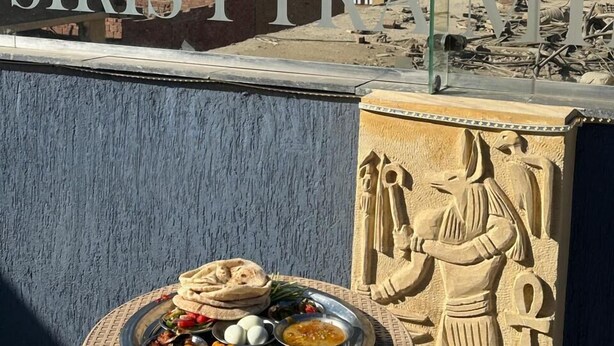 A dining table with a variety of dishes, a pyramid in the background, and a wall with hieroglyphics. - Osiris pyramids view inn  (Giza)