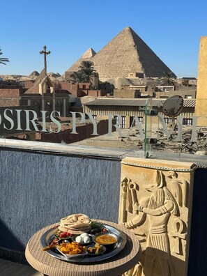 A dining table with a variety of dishes, a pyramid in the background, and a wall with hieroglyphics. - Osiris pyramids view inn  (Giza)