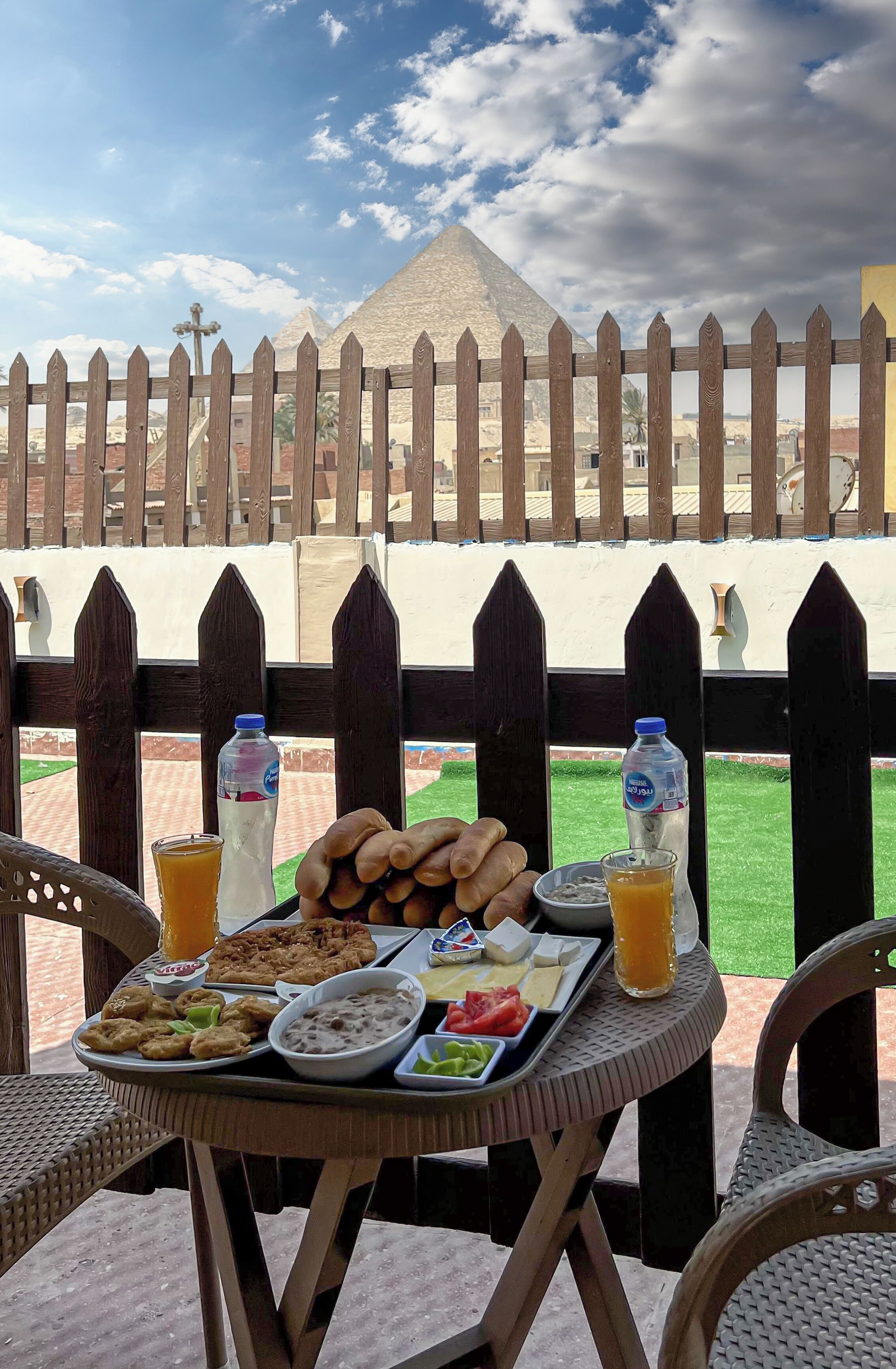 A table with food and drinks on a balcony with a wooden fence and a pyramid in the background.