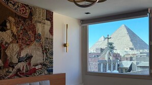 A bedroom with a large bed, a tapestry on the wall, a modern chandelier, and a view of a pyramid through a window. - Osiris pyramids view inn  (Giza)