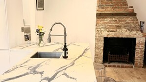 A kitchen with a marble countertop, a modern faucet, a brick fireplace, and a vase with flowers. - No Longer Available (Petworth)
