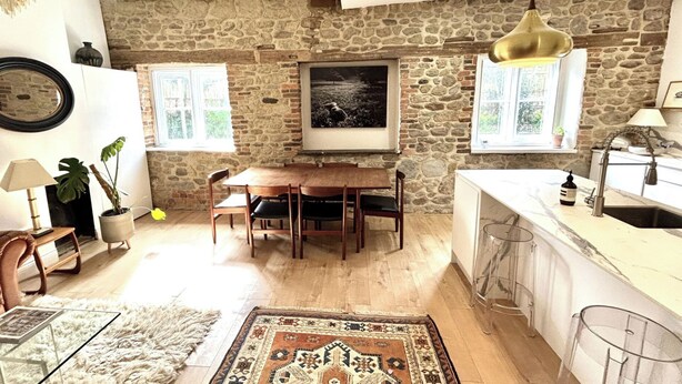 A cozy kitchen with a stone wall, wooden dining table, and a hanging light fixture. - No Longer Available (Petworth)