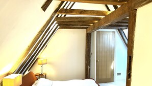 A bedroom with a sloped ceiling, a bed, a bedside table with a lamp, and a door. - No Longer Available (Petworth)