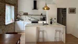 A modern kitchen with a marble island, clear stools, a stone wall, and a hanging pendant light. - No Longer Available (Petworth)
