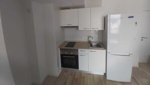 Une cuisine compacte avec des meubles blancs, un four encastré, un évier et un réfrigérateur.