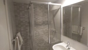 Une salle de bain moderne avec une douche à parois de verre, un lavabo blanc et un grand miroir.