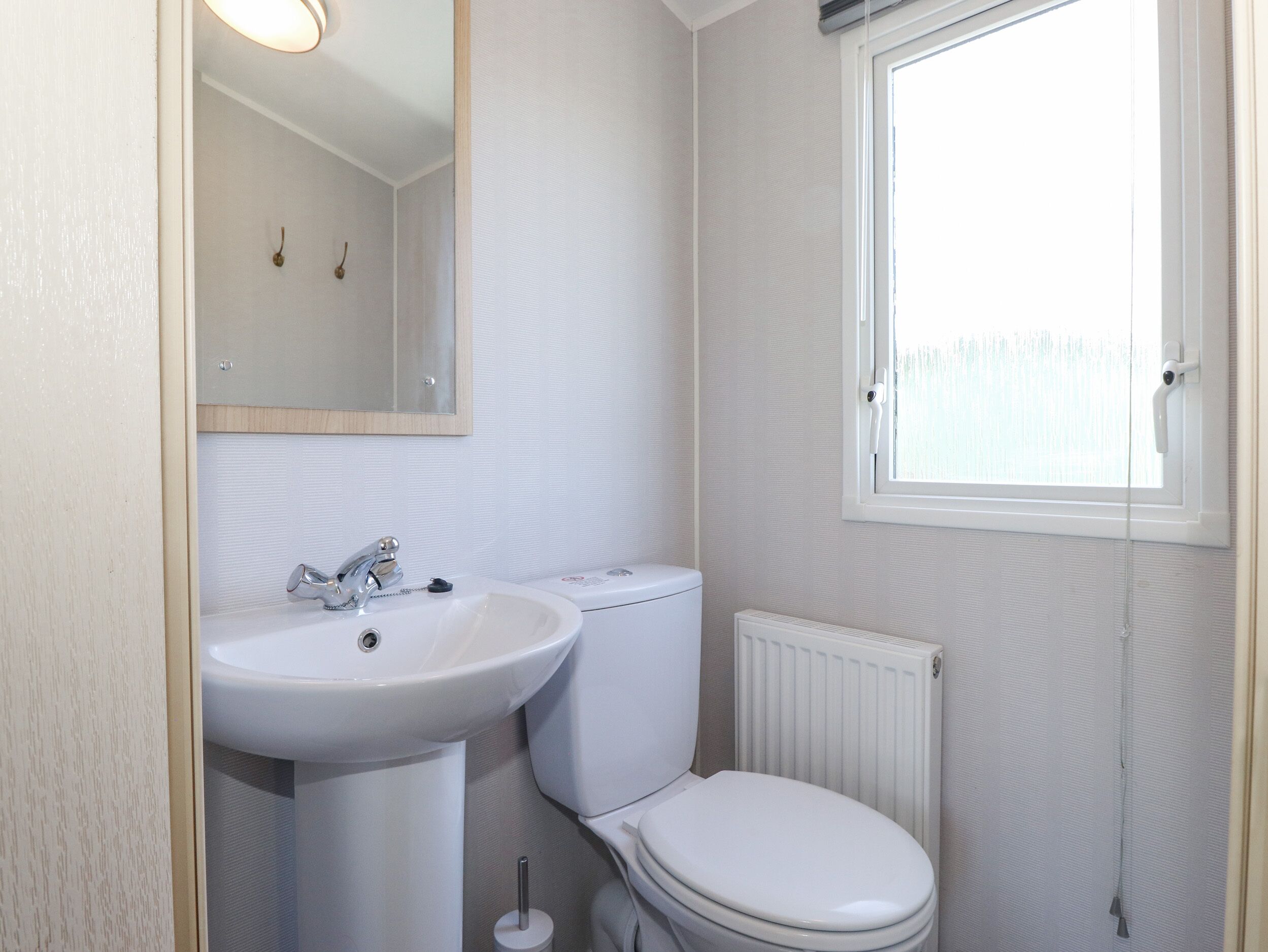 Ein Badezimmer mit weißem Waschbecken, Toilette und einem Fenster mit Blick ins Freie.