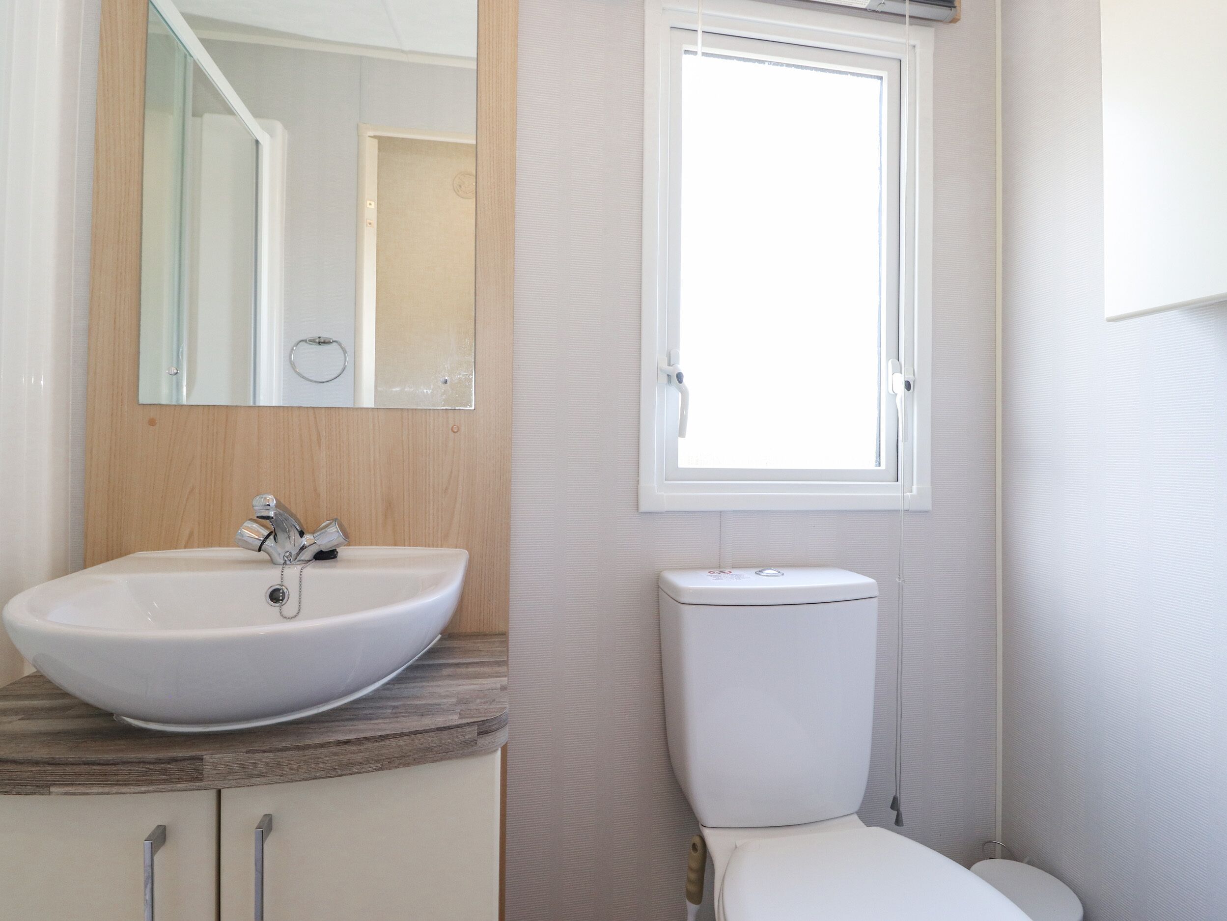 A bathroom with a white sink, a mirror, a toilet, and a window.