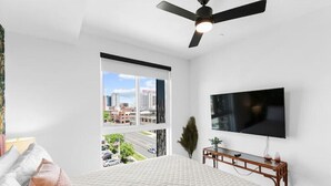 A bedroom with a large bed, a ceiling fan, a TV mounted on the wall, and a window offering a city view. - Centrally located - 2 min walk to UAB (Birmingham)