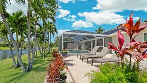 A covered outdoor area with a pool, lounge chairs, and tropical plants. - Relaxing Water views and close to dining, shopping and beaches (Cape Coral)