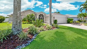 A residential house with a well-maintained lawn, palm trees, and a bicycle parked outside. - Relaxing Water views and close to dining, shopping and beaches (Cape Coral)