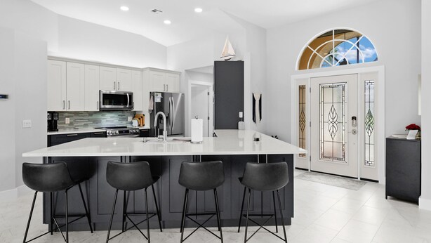 A modern kitchen with white cabinetry, a large island with bar stools, stainless steel appliances, and a decorative sail on the ceiling. - Relaxing Water views and close to dining, shopping and beaches (Cape Coral)