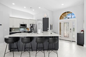 A modern kitchen with white cabinetry, a large island with bar stools, stainless steel appliances, and a decorative sail on the ceiling. - Relaxing Water views and close to dining, shopping and beaches (Cape Coral)