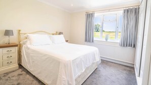 A bedroom with a bed, bedside table, lamp, and a window with curtains. - Long Lane Stables Lodge. Spacious Country Retreat (Penselwood)